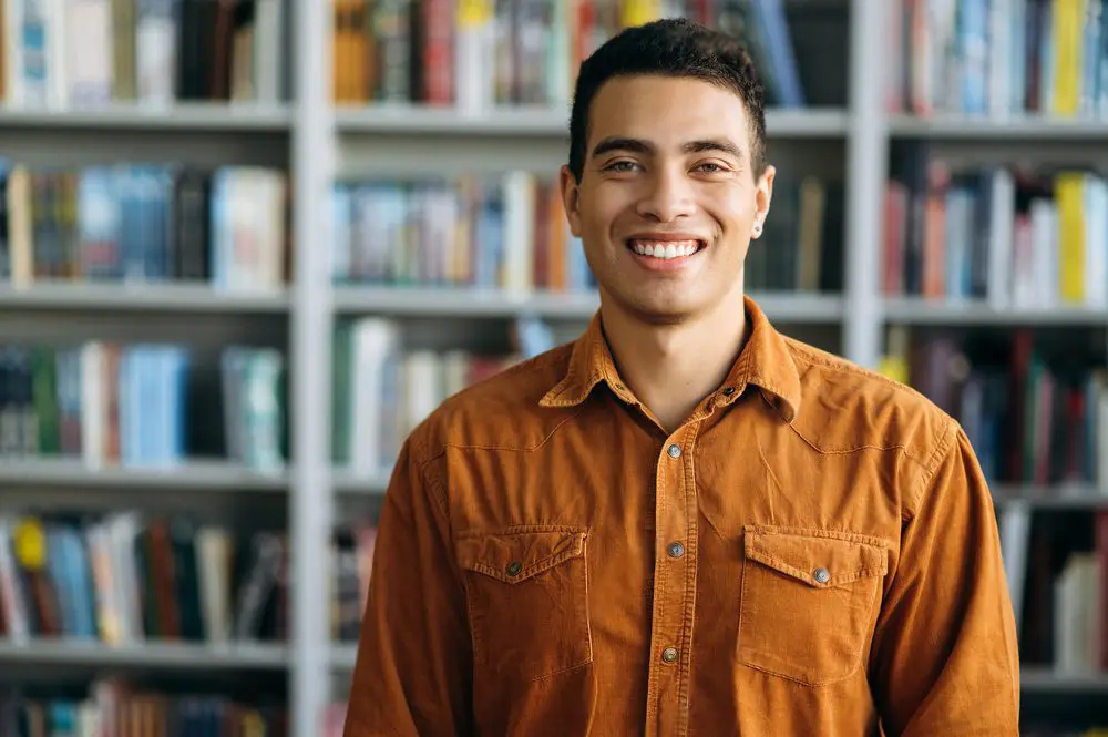 Young man in orange shirt with library books in the background.