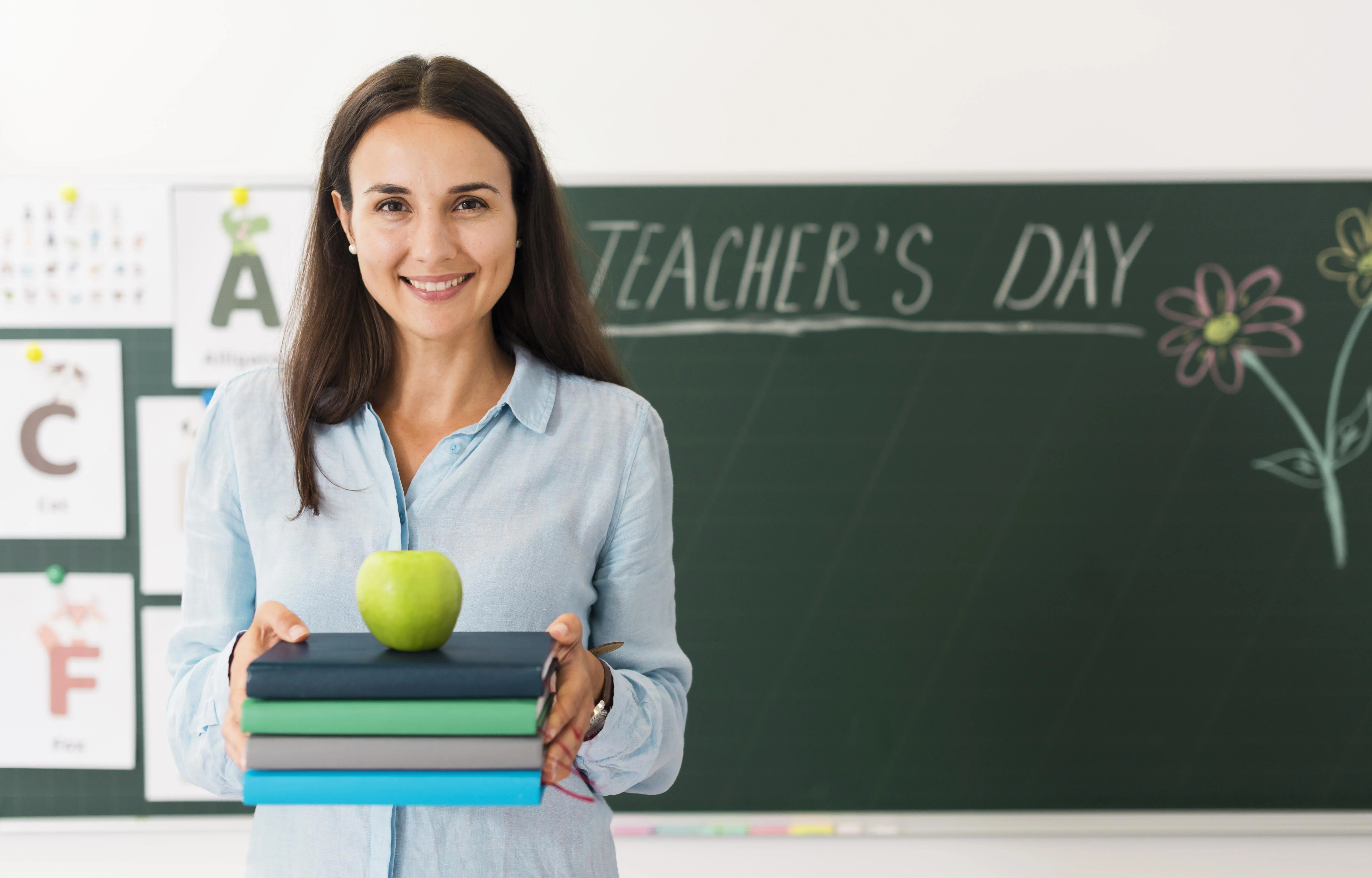 Smiling teacher holding a bunch of books and an apple with copy space.