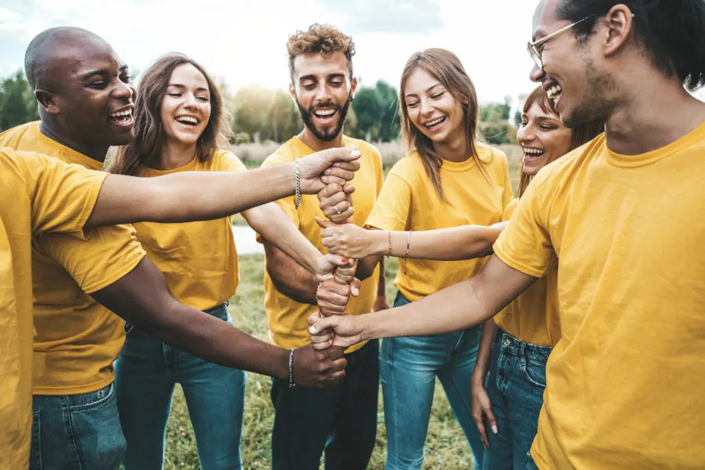 Smiling group of diverse college students in matching yellow shirts joining hands outdoors, symbolizing teamwork, leadership, and community service at Florida National University