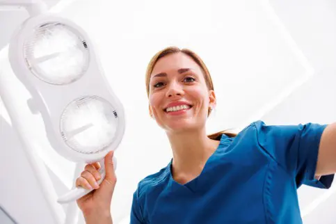 dental assistant looking down on the camera holding dental chair lights