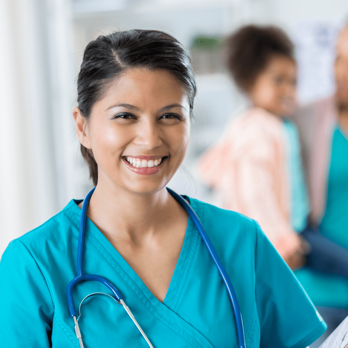 A female nurse is smiling while holding a stethoscope.