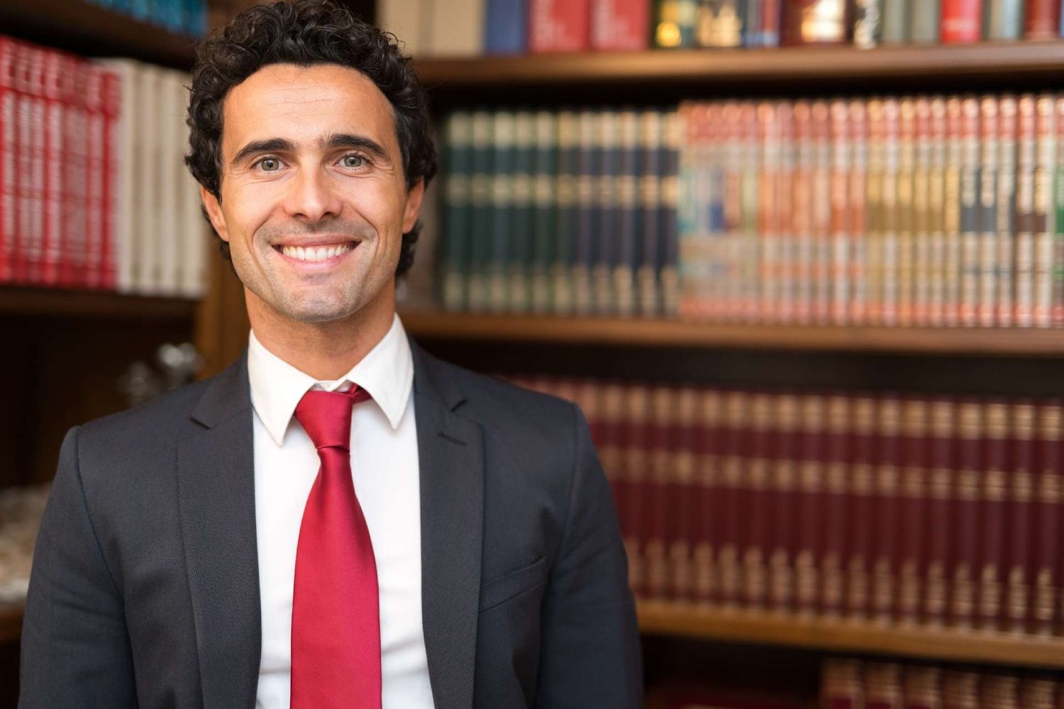 Confident lawyer exuding professionalism and warmth in his meticulously organized studio. With an approachable smile, he radiates trust and expertise, surrounded by law books and legal documents, creating an atmosphere of competence and dedication to his clients' needs.