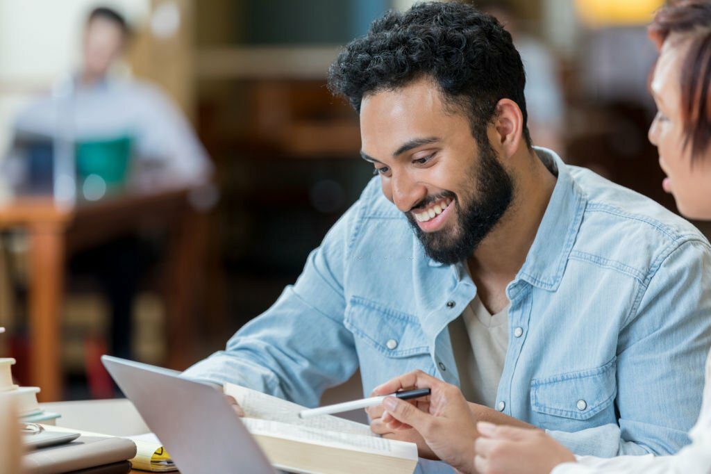 Confident male college student and his friend review information for final exams. They are looking at something in a book.